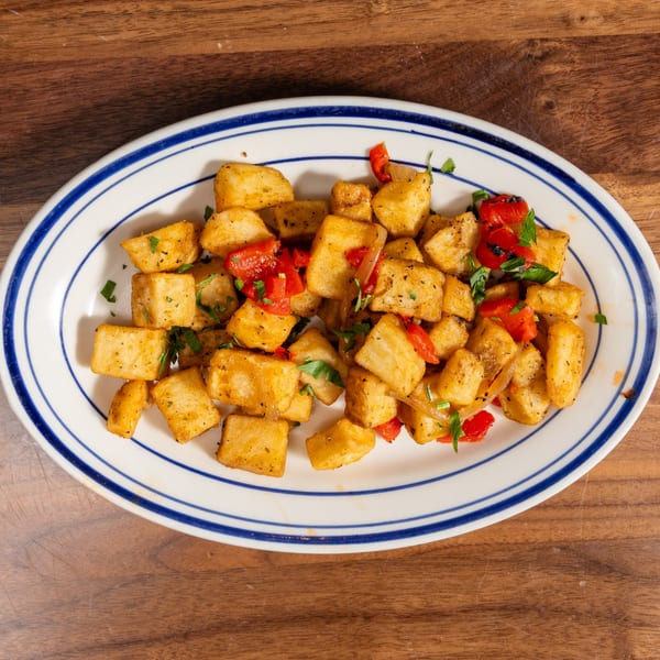 Crispy fried yucca pieces with red peppers, onions, and parsley on a white oval plate.