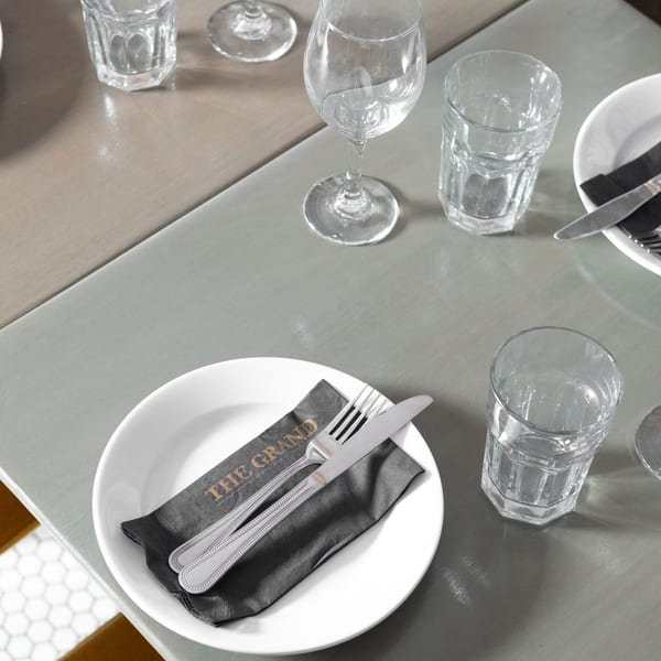 A set table at The Grand restaurant with a white plate, cutlery on a black napkin, and glasses.
