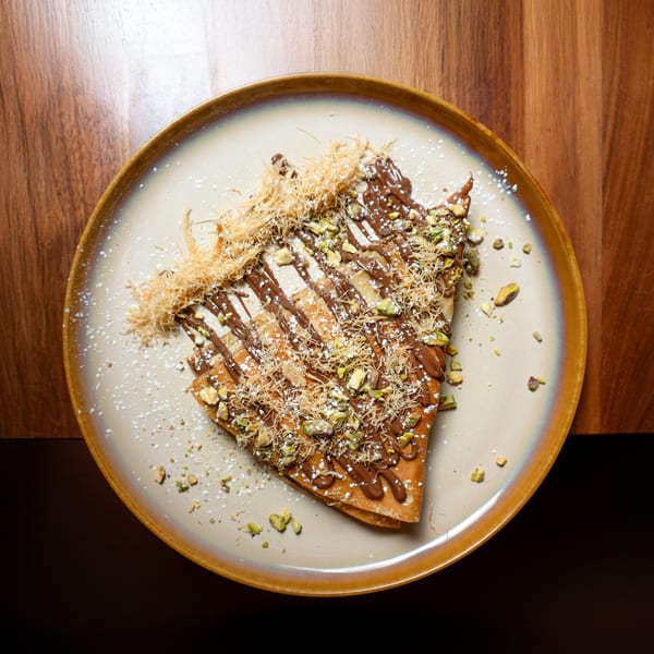 A Grand brunch crepe with chocolate drizzle, pistachios, shredded phyllo, and powdered sugar.