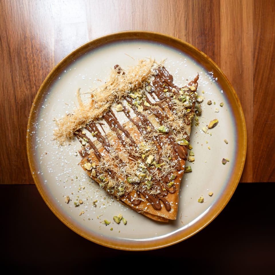 A Grand brunch crepe with chocolate drizzle, pistachios, shredded phyllo, and powdered sugar.