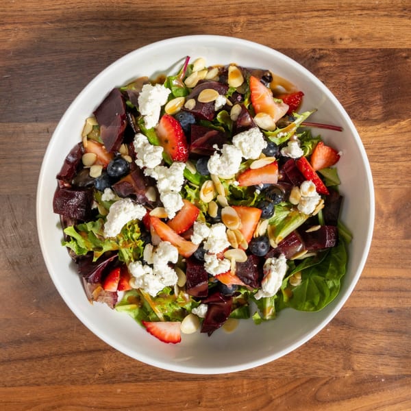 Overhead view of a vibrant salad with mixed greens, strawberries, blueberries, beets, goat cheese, and almonds.