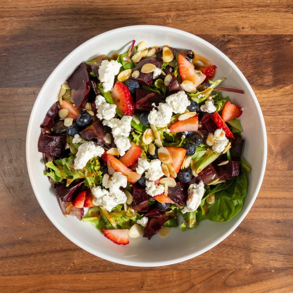 Overhead view of a vibrant salad with mixed greens, strawberries, blueberries, beets, goat cheese, and almonds.