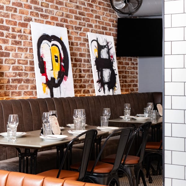 Restaurant interior with brown booths, set tables, brick walls, and modern abstract art.