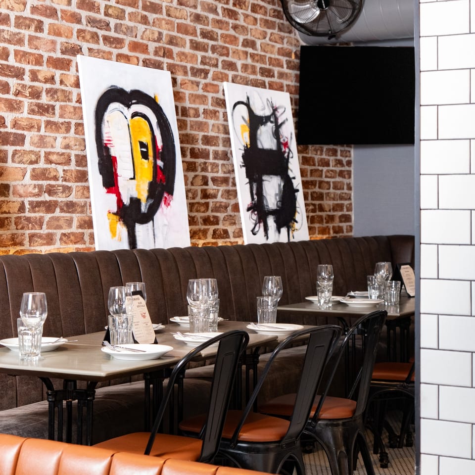 Restaurant interior with brown booths, set tables, brick walls, and modern abstract art.