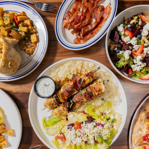 Overhead view of a table laden with various dishes, including chicken skewers, salad, bacon, and breakfast potatoes.