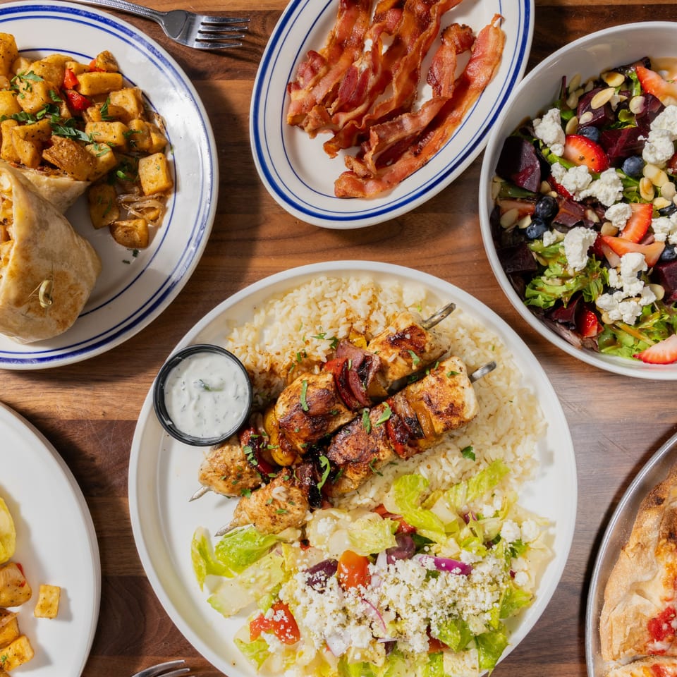 Overhead view of a table laden with various dishes, including chicken skewers, salad, bacon, and breakfast potatoes.