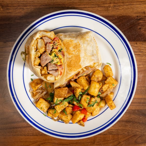 Breakfast burrito with sausage, eggs, and cheese, served with seasoned home fries on a white plate.