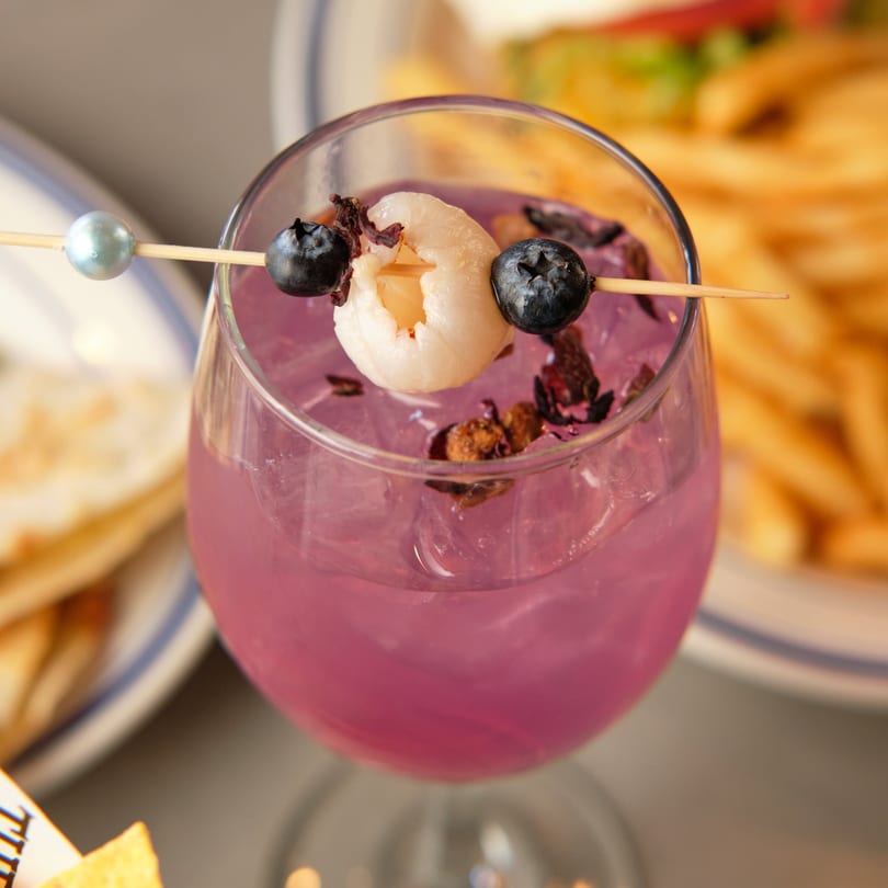 A vibrant purple cocktail garnished with blueberries and a lychee, served at The Grand.