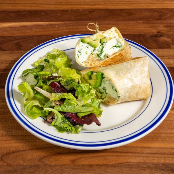 Two halves of a wrap filled with avocado and cream cheese, served with a side salad.