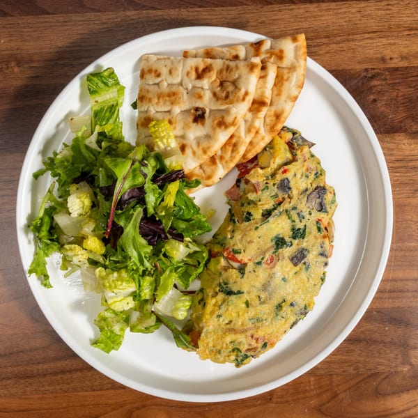 Omelet with olives, tomatoes, and spinach, served with pita bread and a side salad.