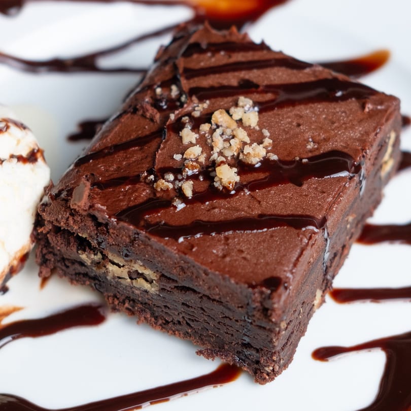 Rich chocolate brownie with nuts, chocolate drizzle, and a scoop of vanilla ice cream.