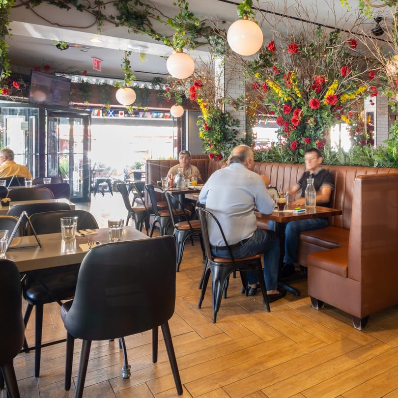 Restaurant interior with patrons dining at tables and booths, adorned with hanging greenery and floral arrangements.