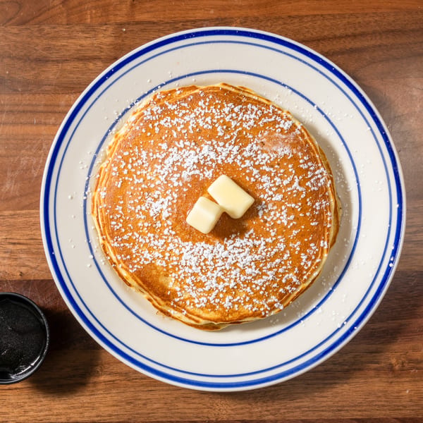 Overhead view of a stack of pancakes with butter and powdered sugar on a white plate with blue stripes.