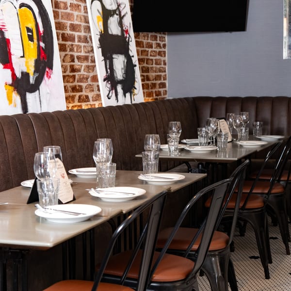 Restaurant interior with set tables, brown booth seating, brick wall, and modern art.