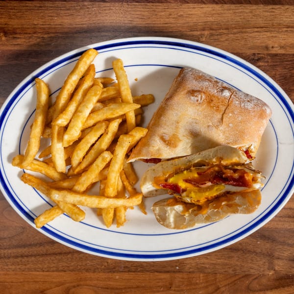 A ciabatta sandwich with melted cheese, bacon, and egg, served with a side of fries.