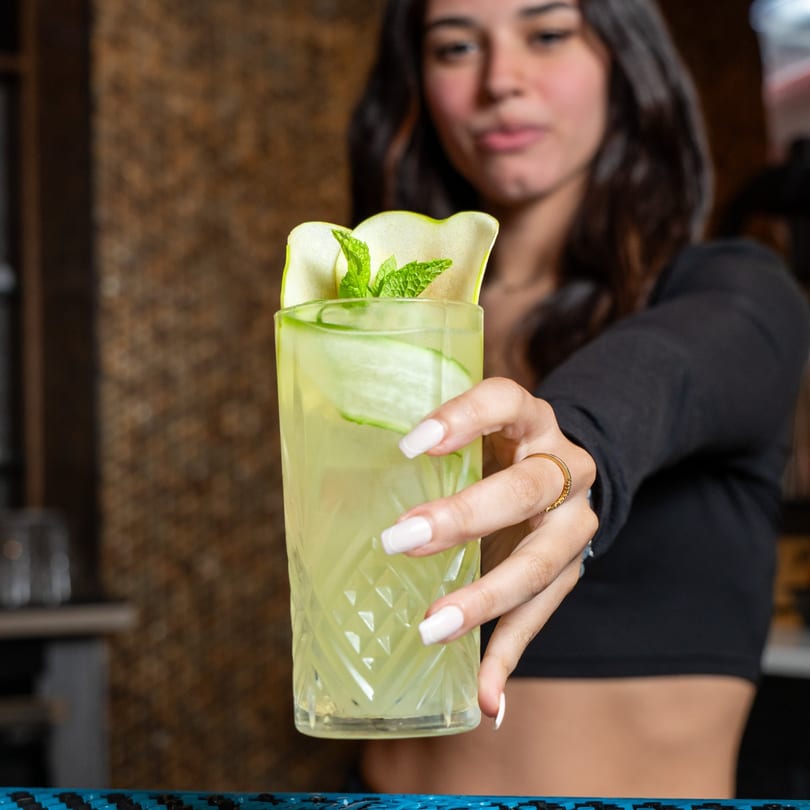 A server at The Grand presents a refreshing green cocktail garnished with cucumber and mint.