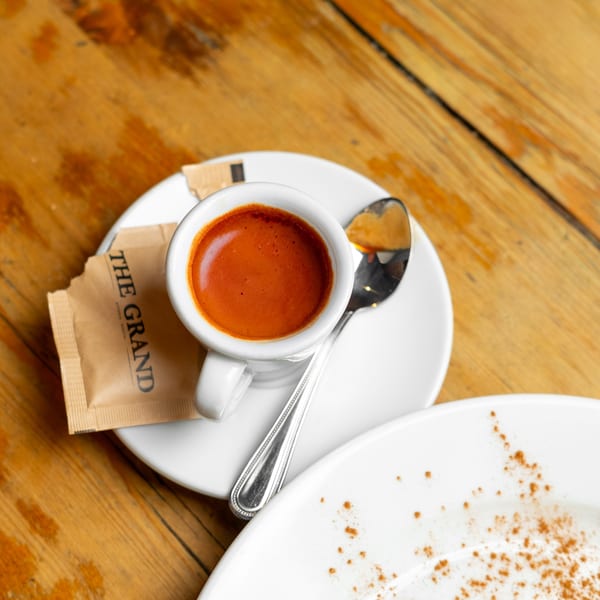 A white espresso cup with a spoon and a sugar packet on a wooden table.