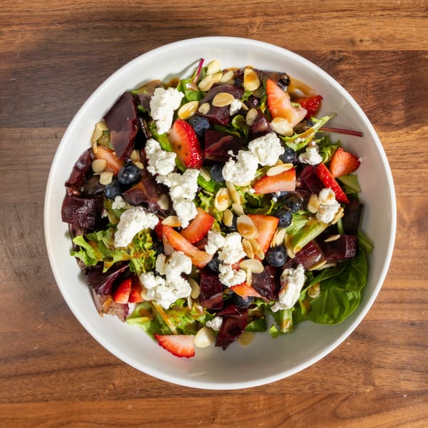 Overhead view of a vibrant salad with mixed greens, beets, strawberries, blueberries, goat cheese, and almonds.