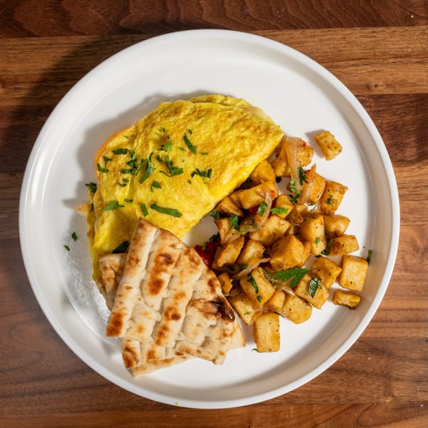 Omelet with parsley, home fries with onions and peppers, and flatbread on a white plate.
