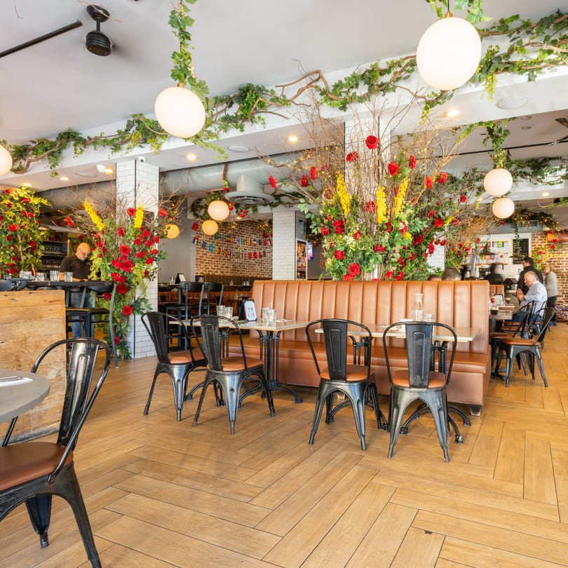 A restaurant interior with brown leather booths, black metal chairs, and lush floral decorations with red roses.