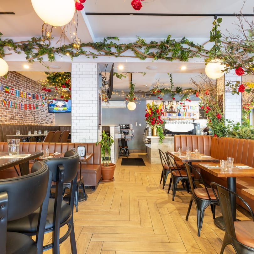 Restaurant interior with brown booths, wooden tables, black chairs, and lush green and red floral decor.