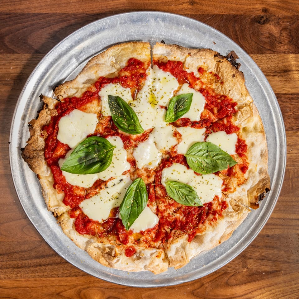 A freshly baked Margherita pizza with melted mozzarella, red sauce, basil, and olive oil.