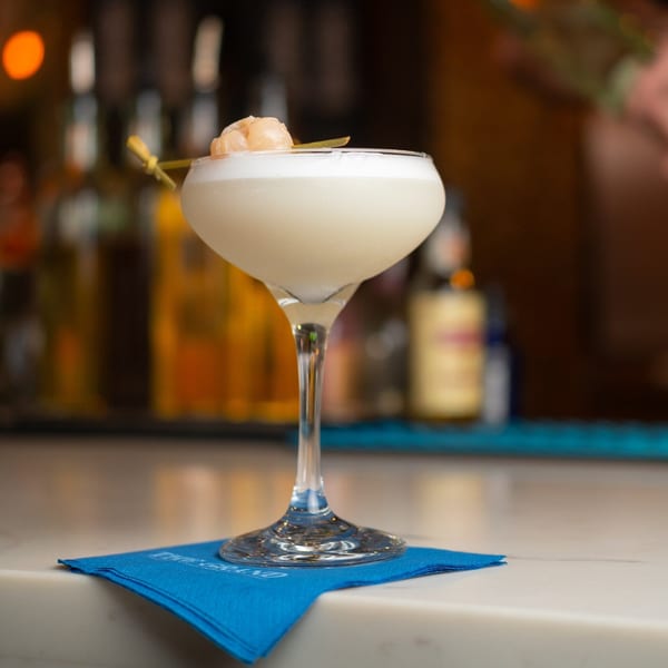 A Grand brunch cocktail, garnished with lychee, sits on a blue napkin at a bar.