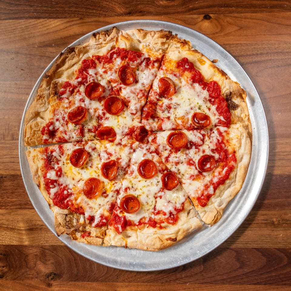 A whole pepperoni pizza, cut into slices, on a metal pan over a wooden table.