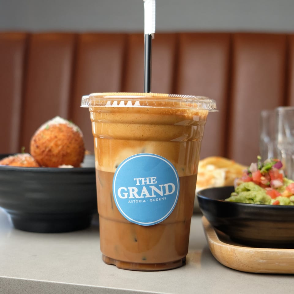 Iced coffee with "The Grand" logo, alongside bowls of arancini and guacamole with pico de gallo.