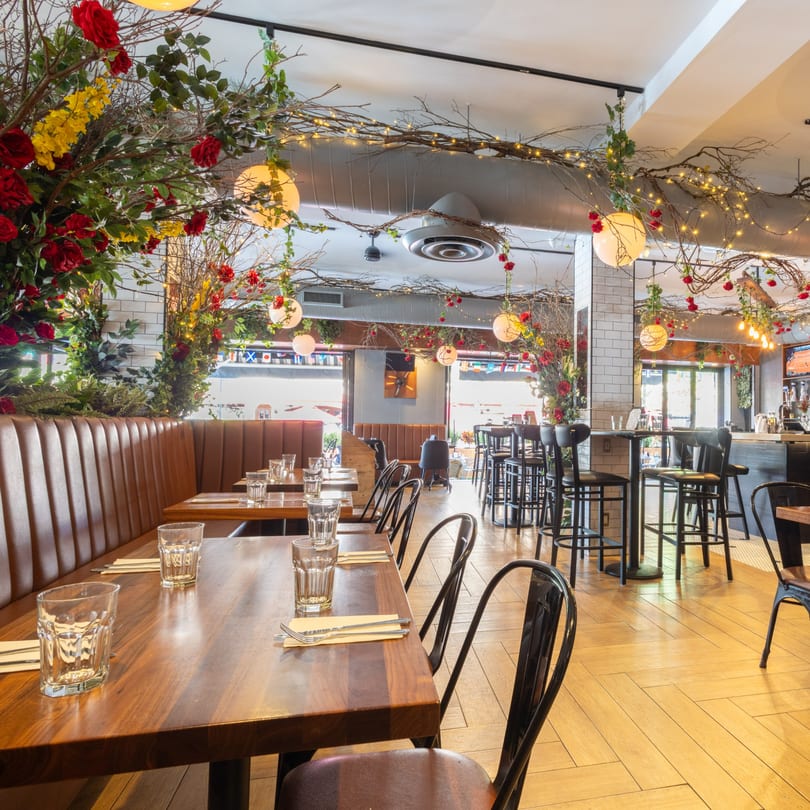 Restaurant interior with wooden tables, brown booths, and branches with red and yellow flowers overhead.