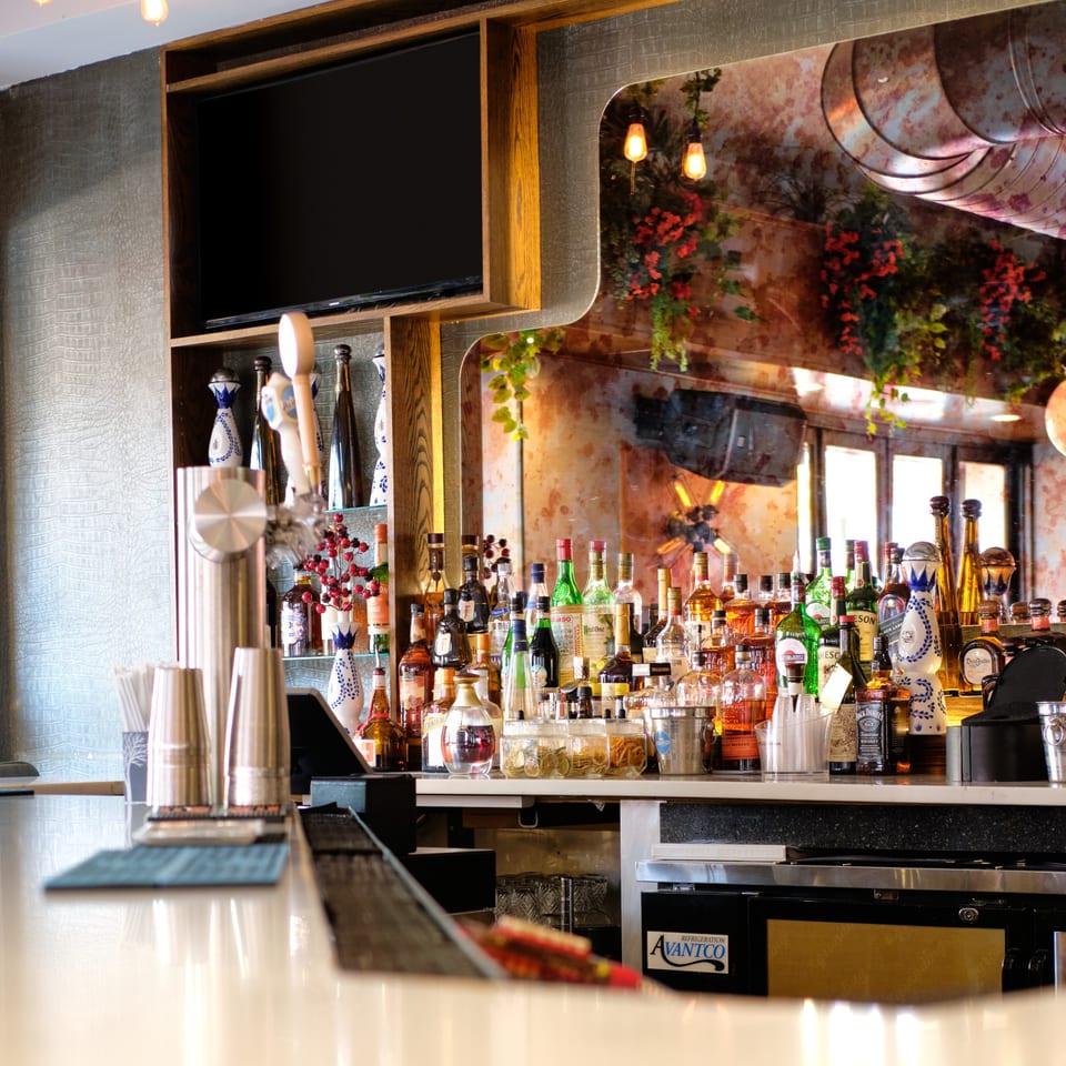 A well-stocked bar with various liquor bottles, shakers, and a TV screen above.